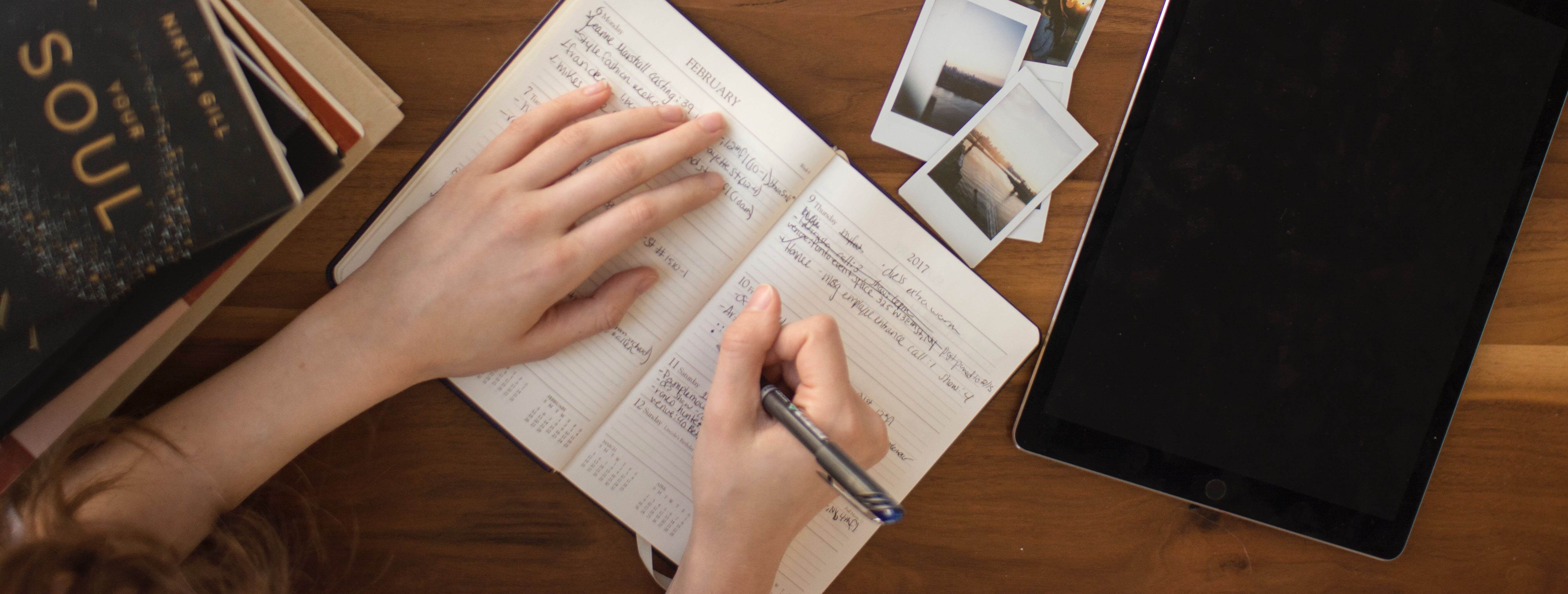 Advérbios - imagem de uma mesa com um caderno aberto e alguém escrevendo.