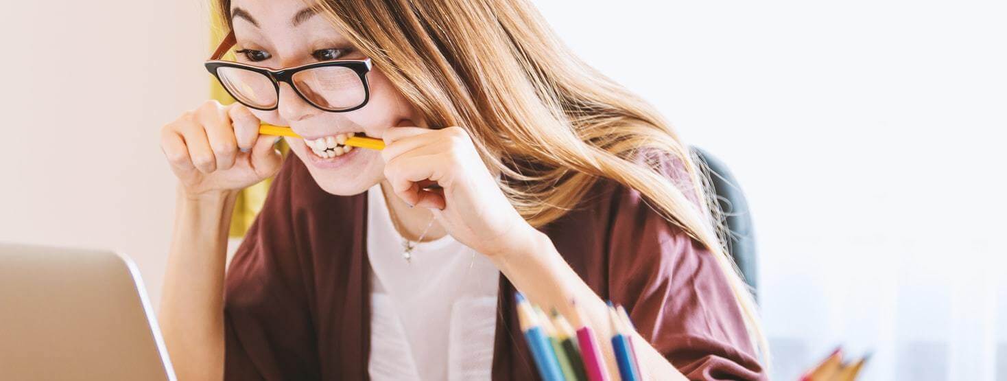 Palavras homófonas e homógrafas: imagem de uma menina mordendo o lápis e olhando para o notebook.
