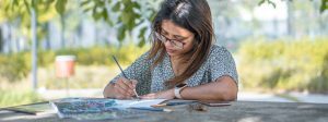 conectivos para redação: imagem de uma mulher escrevendo em um caderno ao ar livre