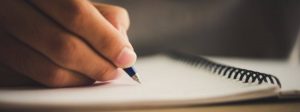 Modelo de redação para concurso: mão sobre caderno escrevendo com uma caneta.