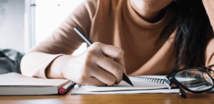 Conectivos de conclusão: imagem de uma estudante escrevendo em seu caderno.