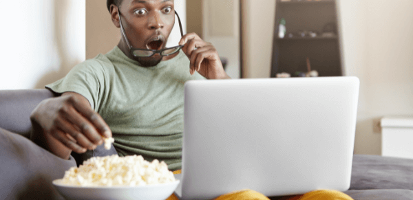 Filmes para citar na redação: imagem de um estudante assistindo a um filme pelo notebook e comendo pipoca